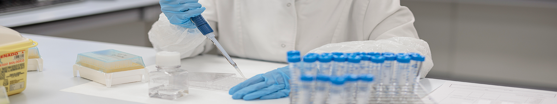 Zatvoren plan znanstvenika u laboratoriju koji nosi rukavice i bijeli mantil, provodi molekularno testiranje koristeći pipetu. Radni prostor je organiziran s epruvetama, posudama i drugim laboratorijskim priborom, što ukazuje na kontrolirano i sterilno okruženje